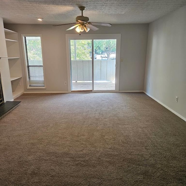 unfurnished living room featuring a fireplace with raised hearth, plenty of natural light, a textured ceiling, and carpet flooring