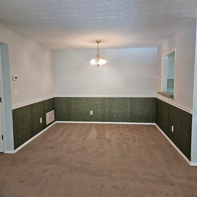 carpeted spare room with a textured ceiling, wainscoting, and visible vents