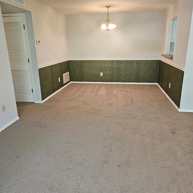 unfurnished room featuring visible vents, wainscoting, a textured ceiling, and carpet flooring