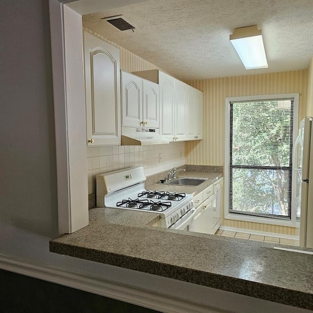 kitchen featuring under cabinet range hood, white appliances, a sink, visible vents, and white cabinets