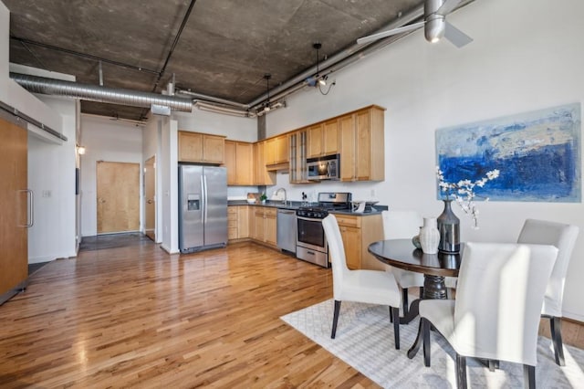 kitchen with light brown cabinetry, light hardwood / wood-style floors, a towering ceiling, appliances with stainless steel finishes, and sink