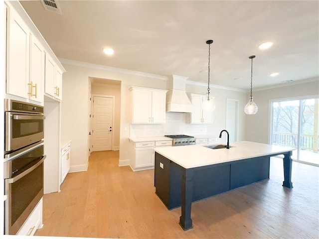 kitchen with sink, premium range hood, pendant lighting, a center island with sink, and white cabinets