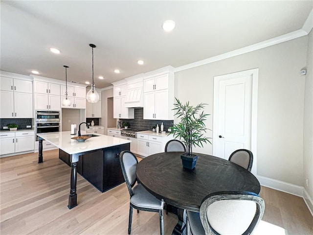 kitchen with white cabinetry, an island with sink, pendant lighting, and light wood-type flooring