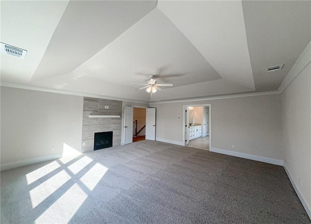 unfurnished living room featuring ceiling fan, ornamental molding, a tray ceiling, light colored carpet, and a tiled fireplace