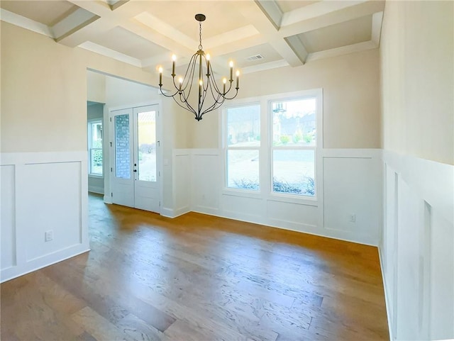 unfurnished dining area with a wealth of natural light, beamed ceiling, coffered ceiling, and an inviting chandelier