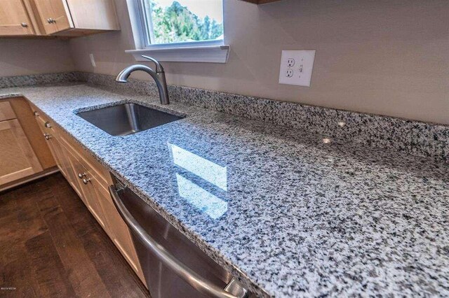 kitchen with dark wood-style floors, brown cabinetry, a sink, light stone countertops, and dishwasher