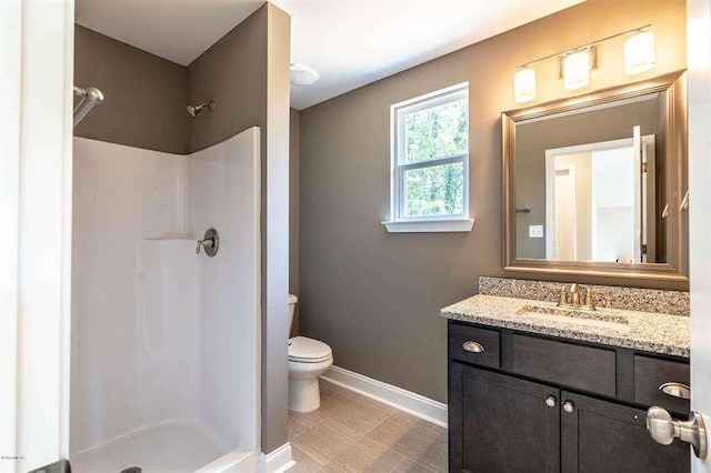 bathroom with a stall shower, baseboards, vanity, and toilet