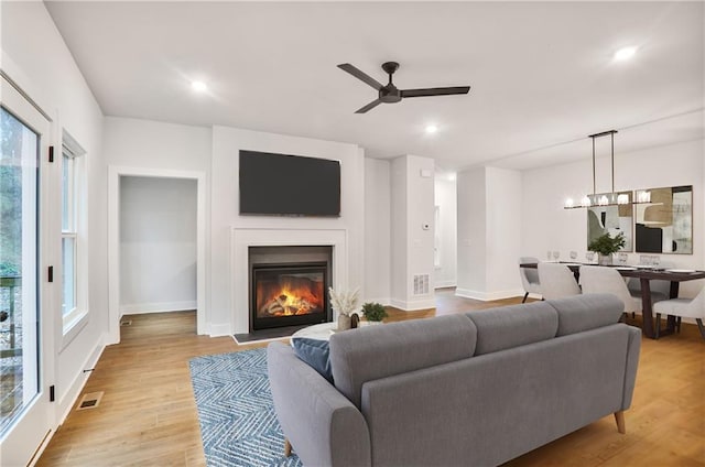 living room with ceiling fan with notable chandelier and light hardwood / wood-style floors