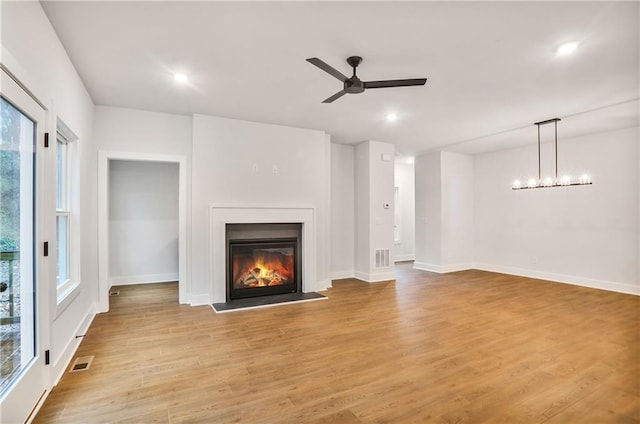 unfurnished living room with a healthy amount of sunlight, ceiling fan with notable chandelier, and light hardwood / wood-style flooring