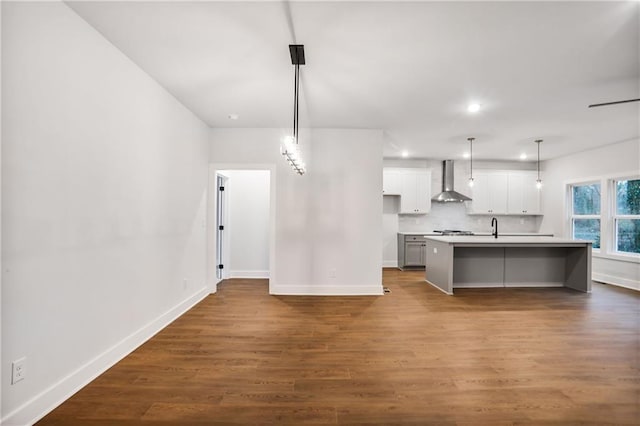 kitchen with an island with sink, white cabinets, hanging light fixtures, hardwood / wood-style flooring, and wall chimney range hood