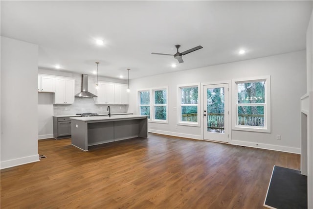 kitchen featuring pendant lighting, white cabinetry, an island with sink, decorative backsplash, and wall chimney exhaust hood