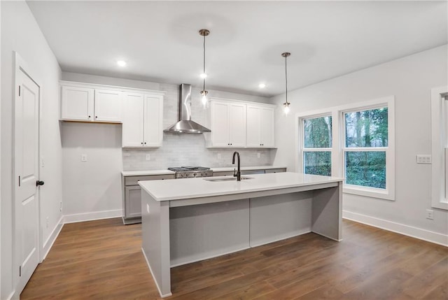 kitchen featuring sink, wall chimney range hood, an island with sink, white cabinets, and decorative light fixtures