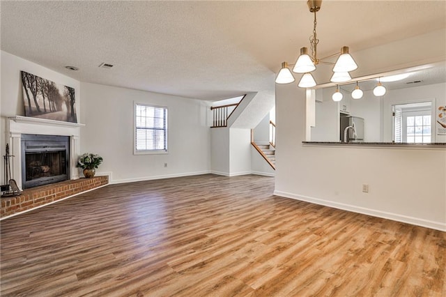 unfurnished living room featuring a fireplace, stairway, a textured ceiling, and wood finished floors