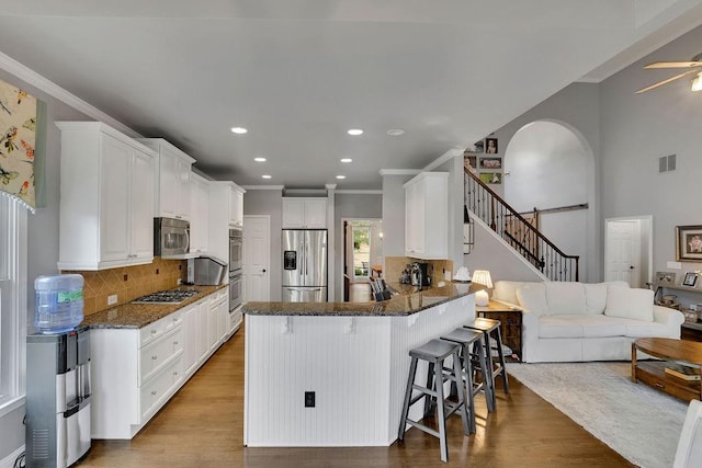 kitchen with white cabinets, a kitchen bar, stainless steel appliances, and hardwood / wood-style flooring