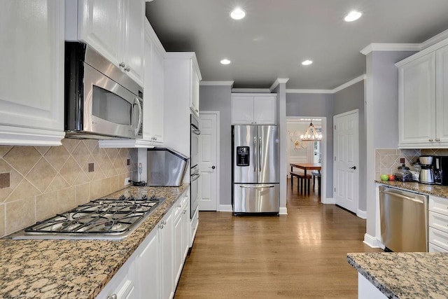 kitchen featuring white cabinets, light wood-type flooring, ornamental molding, light stone counters, and stainless steel appliances