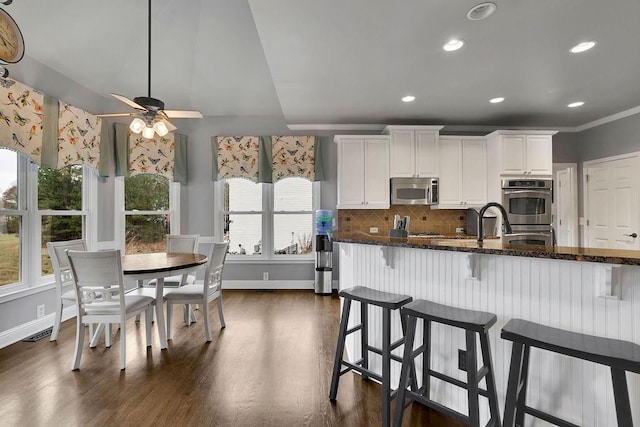 kitchen with dark wood-type flooring, dark stone counters, white cabinets, decorative backsplash, and appliances with stainless steel finishes