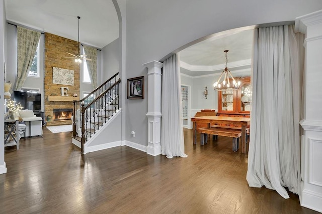 foyer featuring ornate columns, ceiling fan, dark wood-type flooring, a fireplace, and ornamental molding