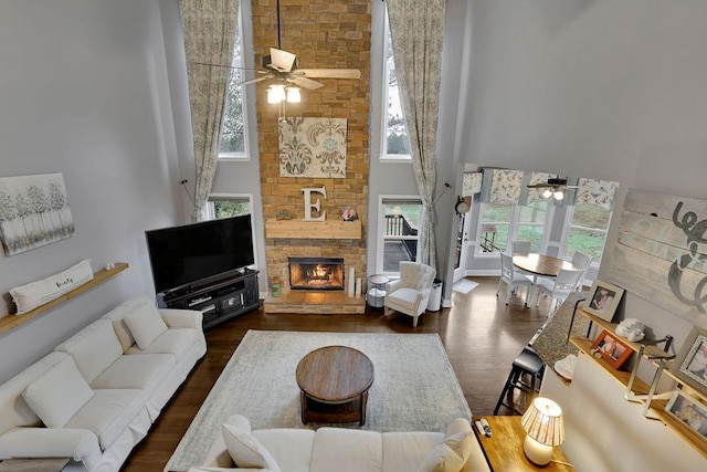 living room with a stone fireplace, ceiling fan, a towering ceiling, and dark hardwood / wood-style floors