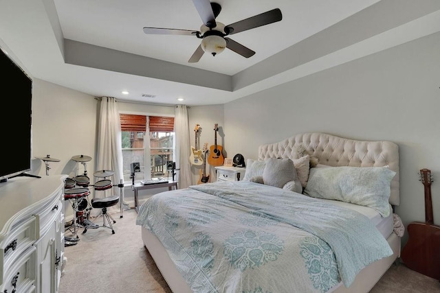 bedroom with ceiling fan, light carpet, and a tray ceiling