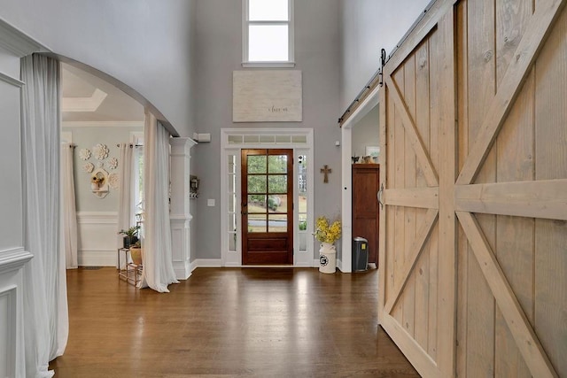 entryway with a towering ceiling, wood-type flooring, a barn door, and ornamental molding