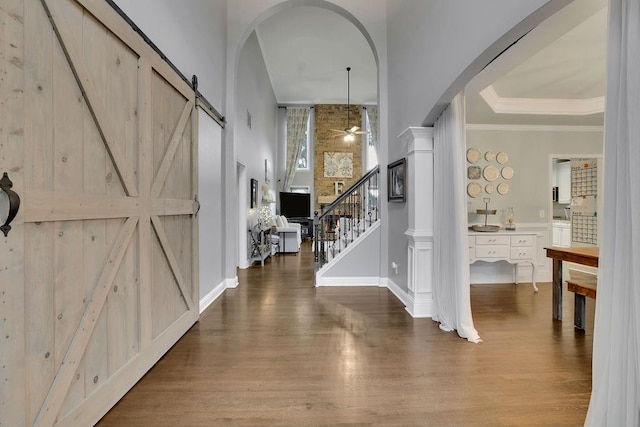 foyer with a high ceiling, ceiling fan, a barn door, ornamental molding, and wood-type flooring