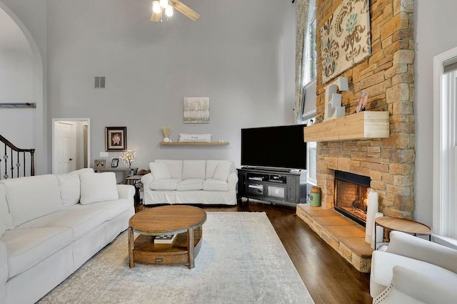 living room with dark hardwood / wood-style floors, ceiling fan, a stone fireplace, and a towering ceiling