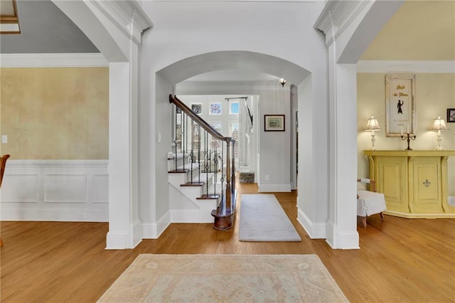 entrance foyer with arched walkways, a wainscoted wall, stairs, and wood finished floors