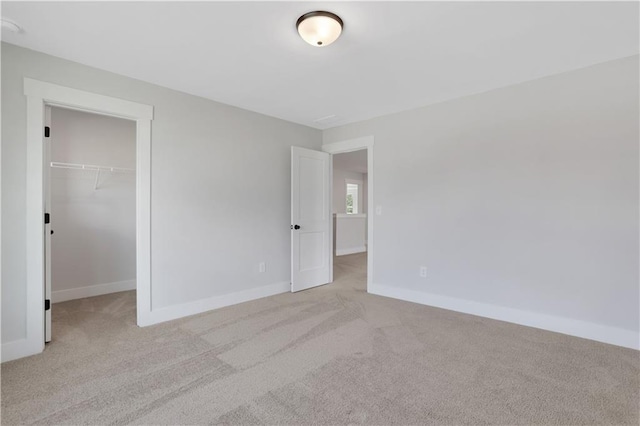 unfurnished bedroom with a spacious closet, baseboards, a closet, and light carpet