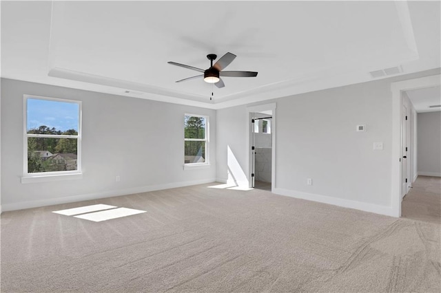 empty room featuring carpet, a tray ceiling, a ceiling fan, visible vents, and baseboards