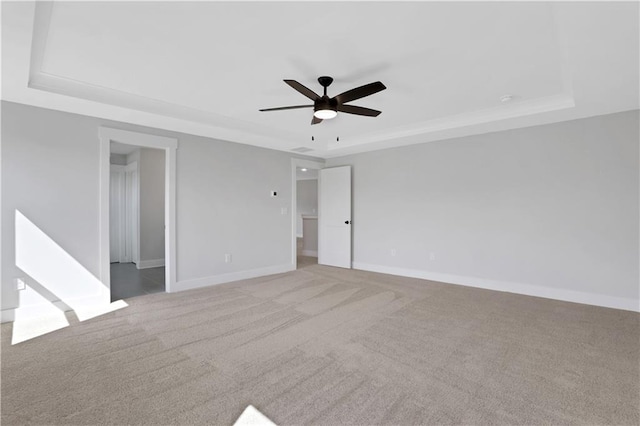 unfurnished room featuring ceiling fan, light colored carpet, and a raised ceiling