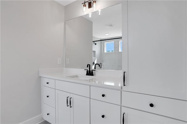bathroom with tiled shower, vanity, and baseboards