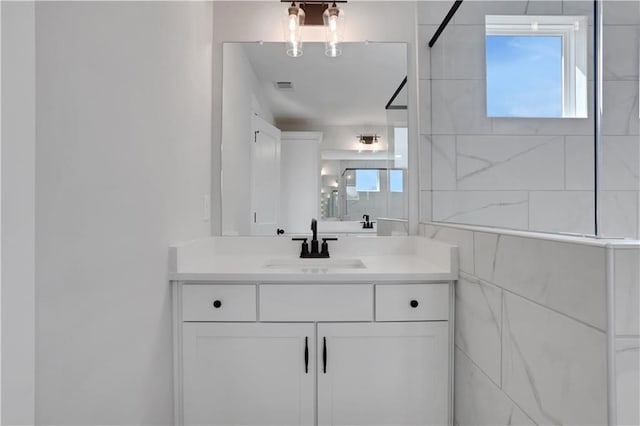 full bath with tiled shower, vanity, and visible vents