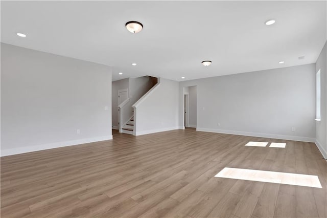 unfurnished living room with light wood-style floors, recessed lighting, baseboards, and stairway