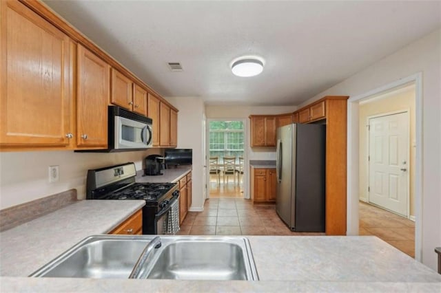 kitchen featuring appliances with stainless steel finishes, a sink, light tile patterned floors, light countertops, and brown cabinetry