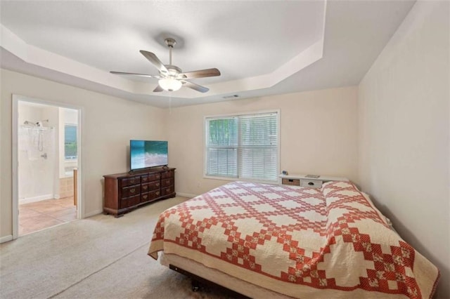 bedroom featuring a raised ceiling, carpet flooring, baseboards, ceiling fan, and ensuite bathroom