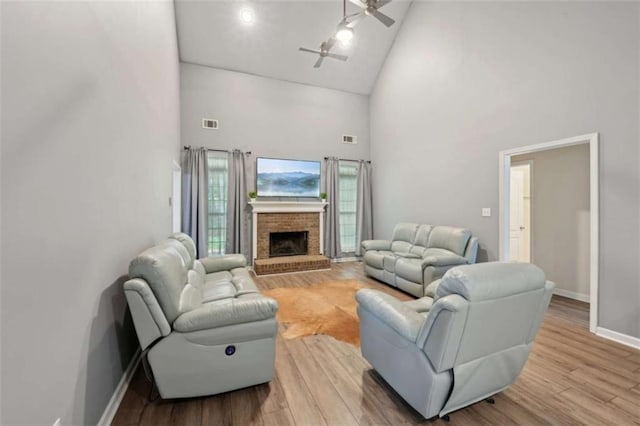 living area with high vaulted ceiling, a ceiling fan, baseboards, a brick fireplace, and light wood-style flooring