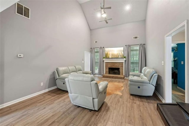 living room with high vaulted ceiling, ceiling fan, a brick fireplace, light wood-style flooring, and baseboards