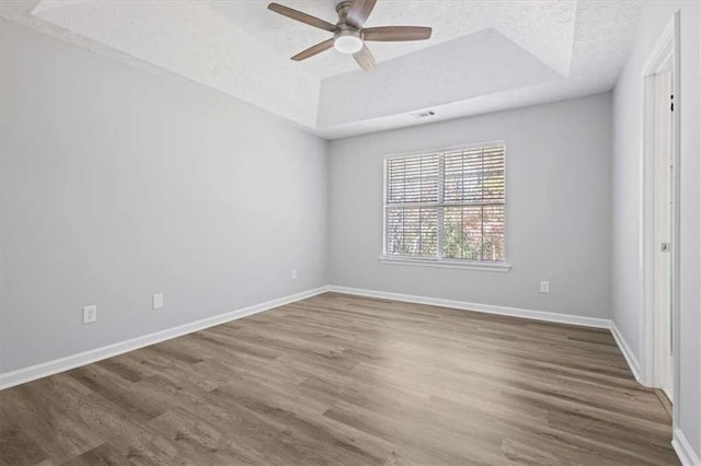 empty room with hardwood / wood-style floors, a textured ceiling, a tray ceiling, and ceiling fan