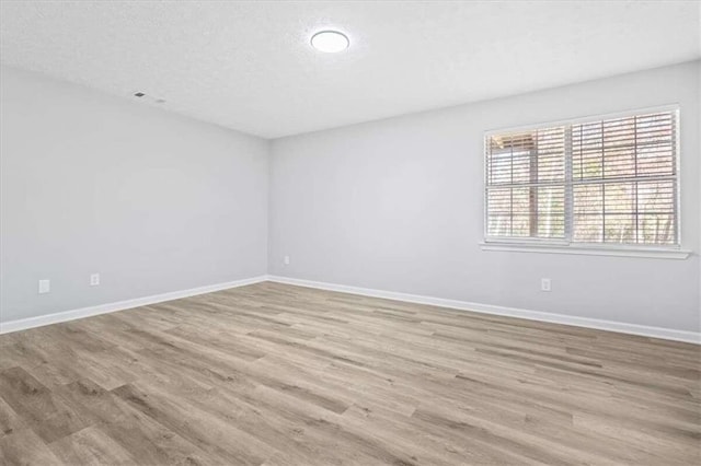 empty room with light wood-type flooring and a textured ceiling