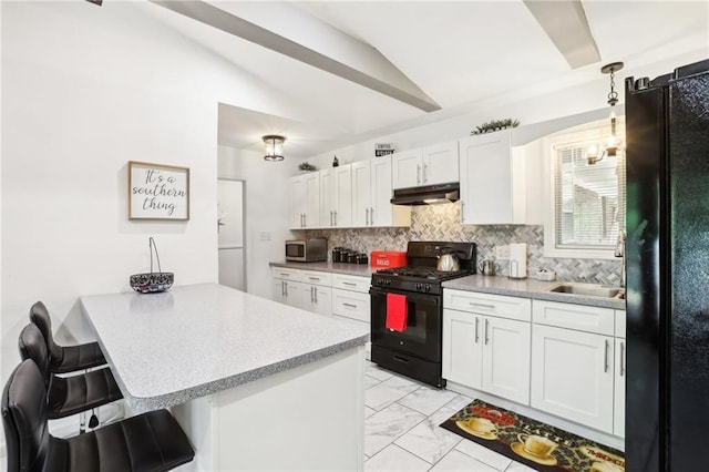 kitchen featuring marble finish floor, black appliances, a peninsula, under cabinet range hood, and a kitchen bar