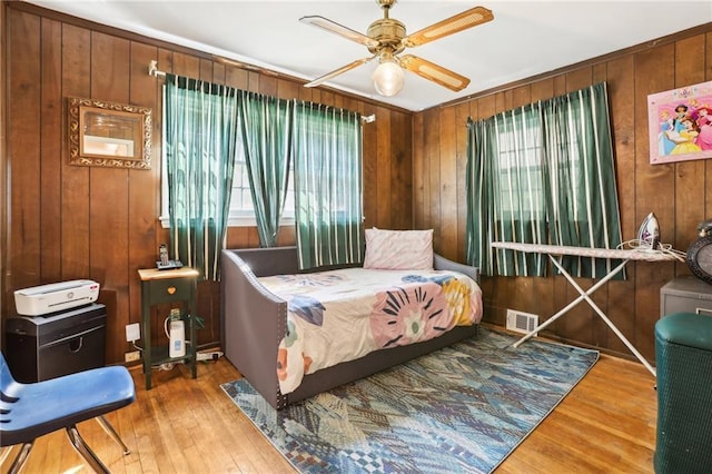 bedroom featuring wood walls, ceiling fan, visible vents, and wood finished floors