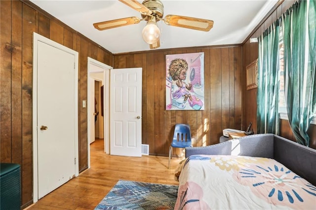 bedroom featuring ornamental molding, wood walls, light wood-style flooring, and a ceiling fan