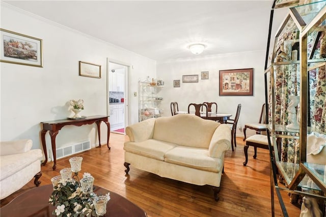 living area with ornamental molding, visible vents, and wood finished floors