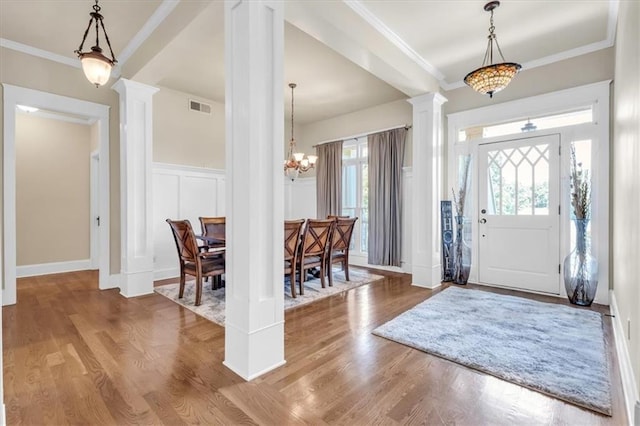 foyer entrance with a chandelier, wood finished floors, a decorative wall, visible vents, and ornate columns
