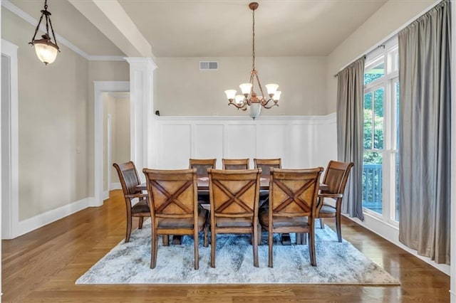 dining space with a chandelier, wainscoting, a decorative wall, visible vents, and ornate columns