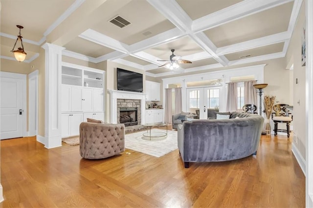 living area with light wood-style flooring, visible vents, beamed ceiling, ceiling fan, and a stone fireplace
