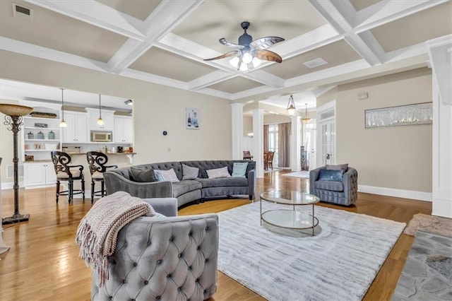 living area featuring decorative columns, light wood-type flooring, visible vents, and ceiling fan