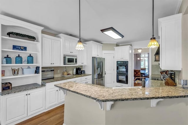 kitchen featuring white cabinetry, stainless steel appliances, light stone countertops, a peninsula, and wood finished floors