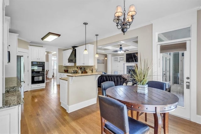 dining area featuring a fireplace, coffered ceiling, ceiling fan with notable chandelier, and light wood finished floors