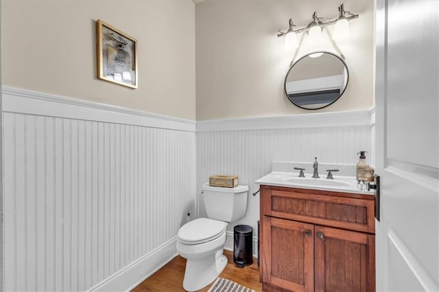 bathroom with a wainscoted wall, toilet, vanity, and wood finished floors